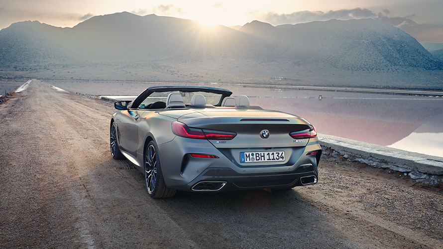 BMW 8 Series Convertible G14 LCI Facelift 2022 rear view with open softtop with hills in the background BMW 8 Series Convertible G14 LCI Facelift 2022 BMW Individual Frozen Pure Grey metallic rear view with open softtop standing on sandy road with hills in the background