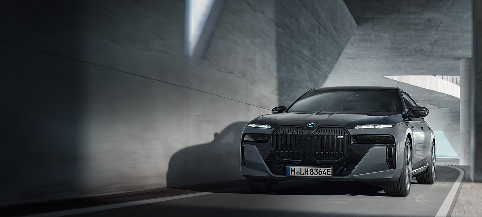 BMW M760e xDrive Sedan G70 M Performance package BMW Individual two-tone Black Sapphire metallic paintwork BMW Individual Dravite Grey metallic three-quarter front view driving on the street