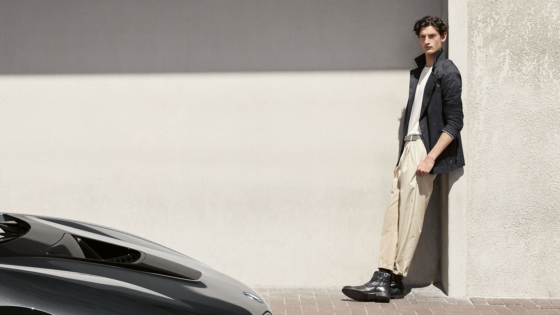 BMW i Collection. The picture shows a man leaning against a wall in a BMW i Jacket, Men from the BMW i Collection.