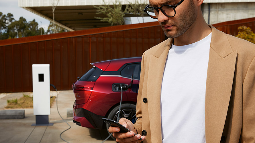 Man with smartphone in front of BMW iX at charging station Man with smartphone in front of BMW iX at charging station